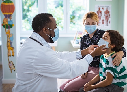 Health care professional examining child, mother looking on