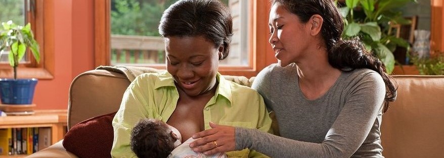 Two adults on couch with breastfeeding baby