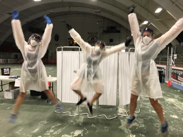 three people in protective garb jump in the air at a public clinic