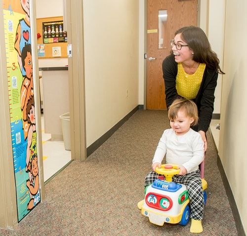 staff helps toddler steer a riding car down a hallway