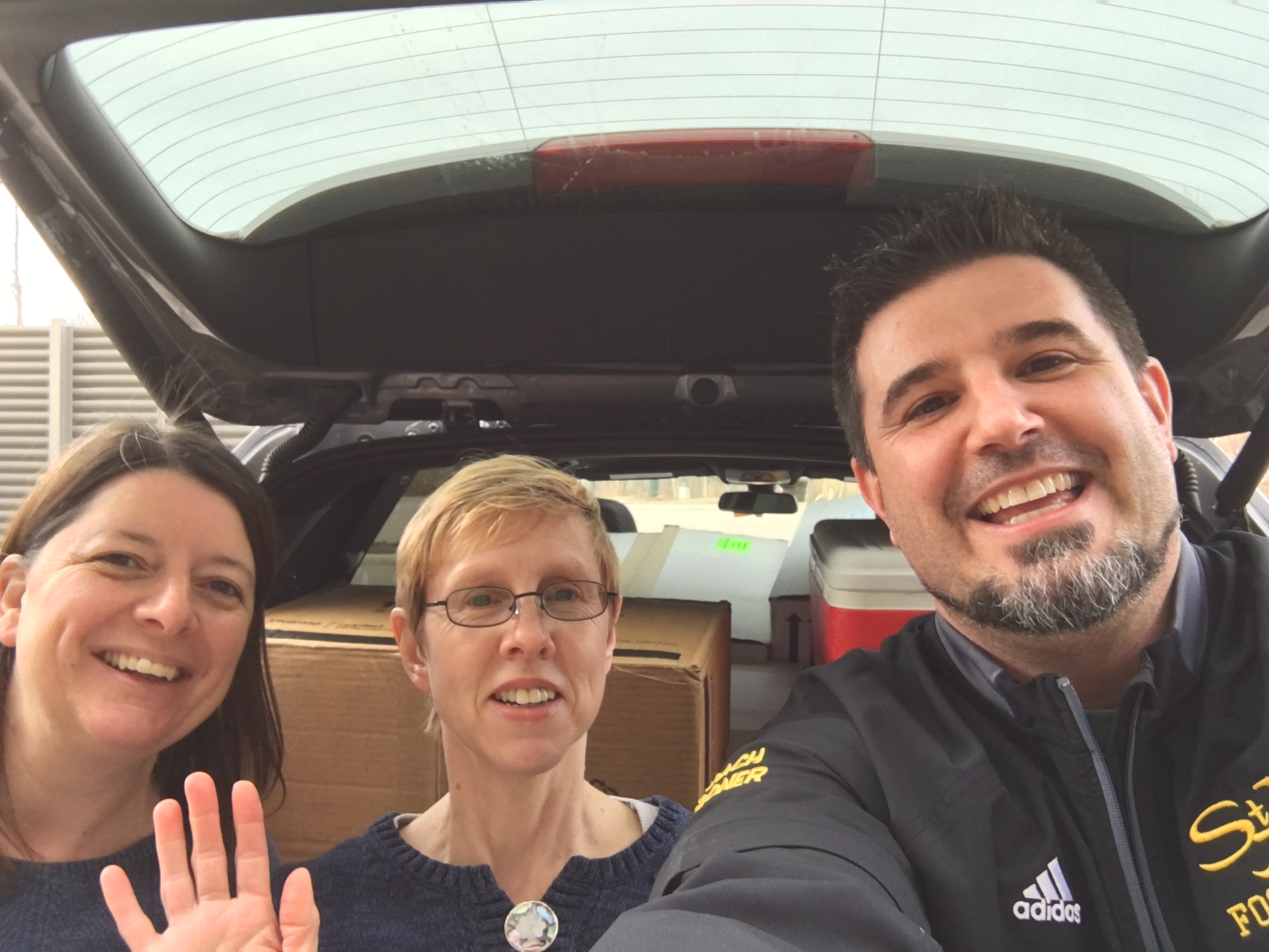 three smiling people standing at back of car