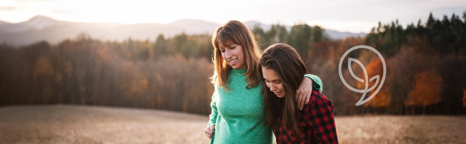 Two women walking in a field with a line of trees in the background