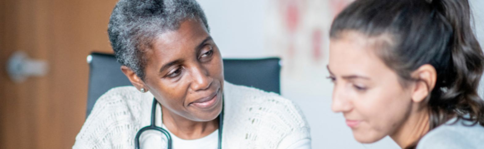 health care worker with a stethoscope and laptop talking with a woman and holding her hand