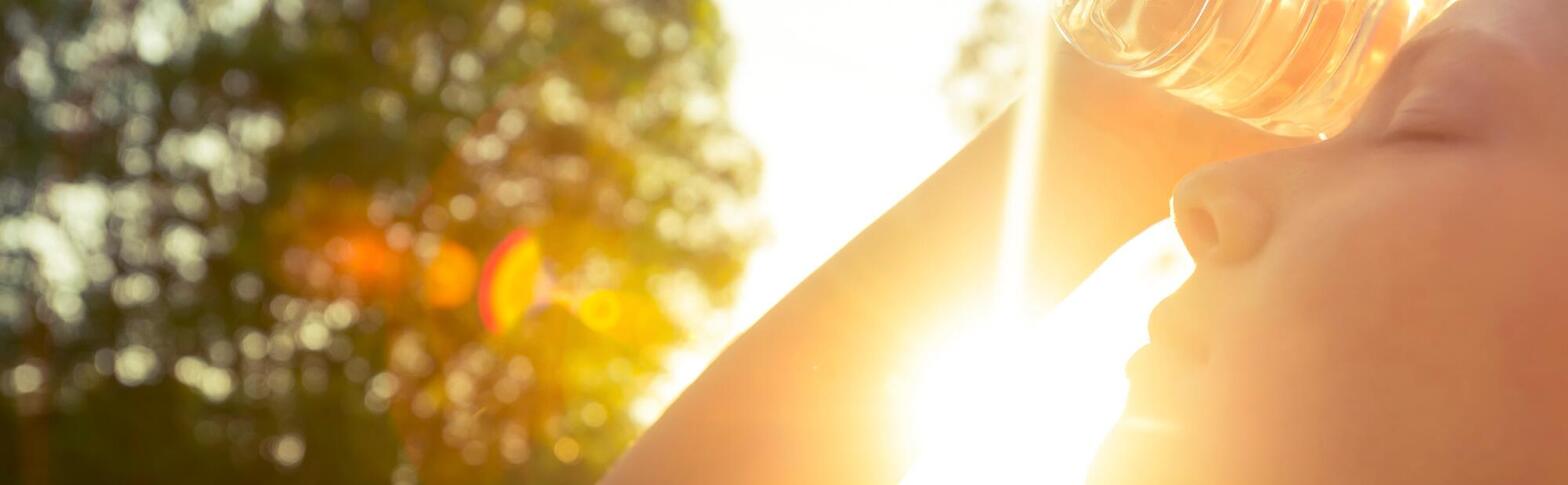 person holding water bottle to head with sun shining