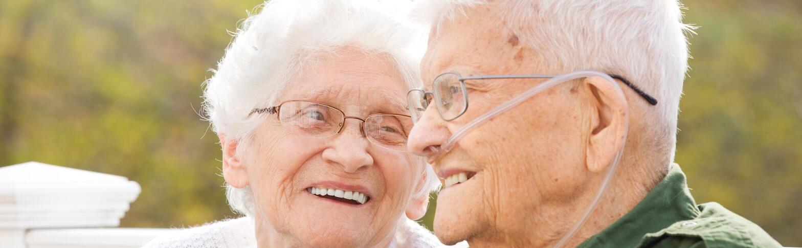 senior couple sitting outside - one with oxygen