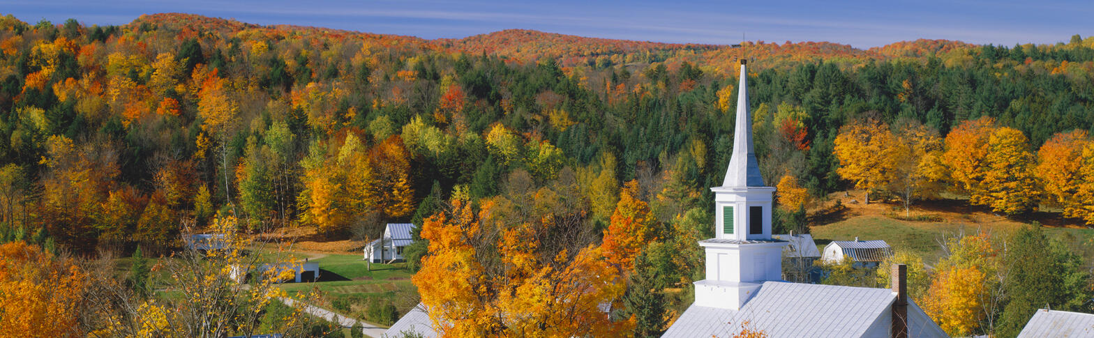 A white church overlooking surrounding hills in foliage season.