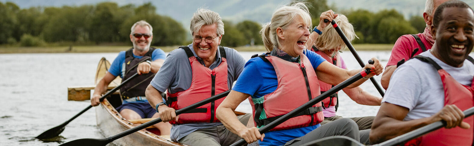 A group of seniors laughing and paddling a boat.