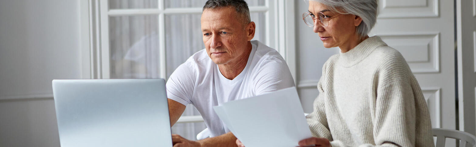 two older people looking at paperwork, computer