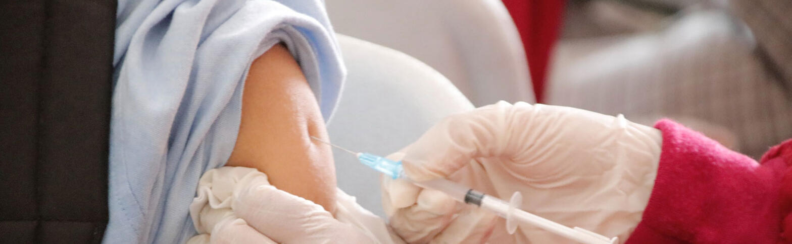 Gloved hands insert vaccine into a young person's arm