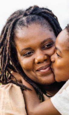A woman smiling and being kissed on the cheek by her young child