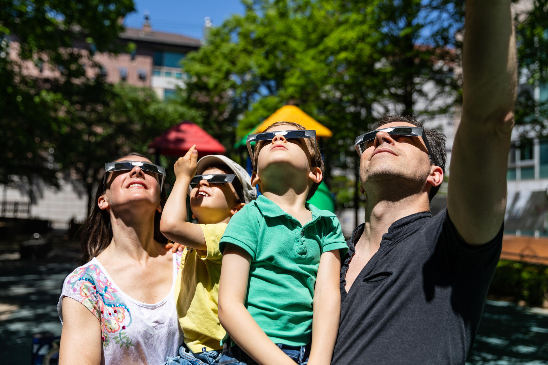 Parents and kids wearing eclipse glasses looking up at an eclipse.
