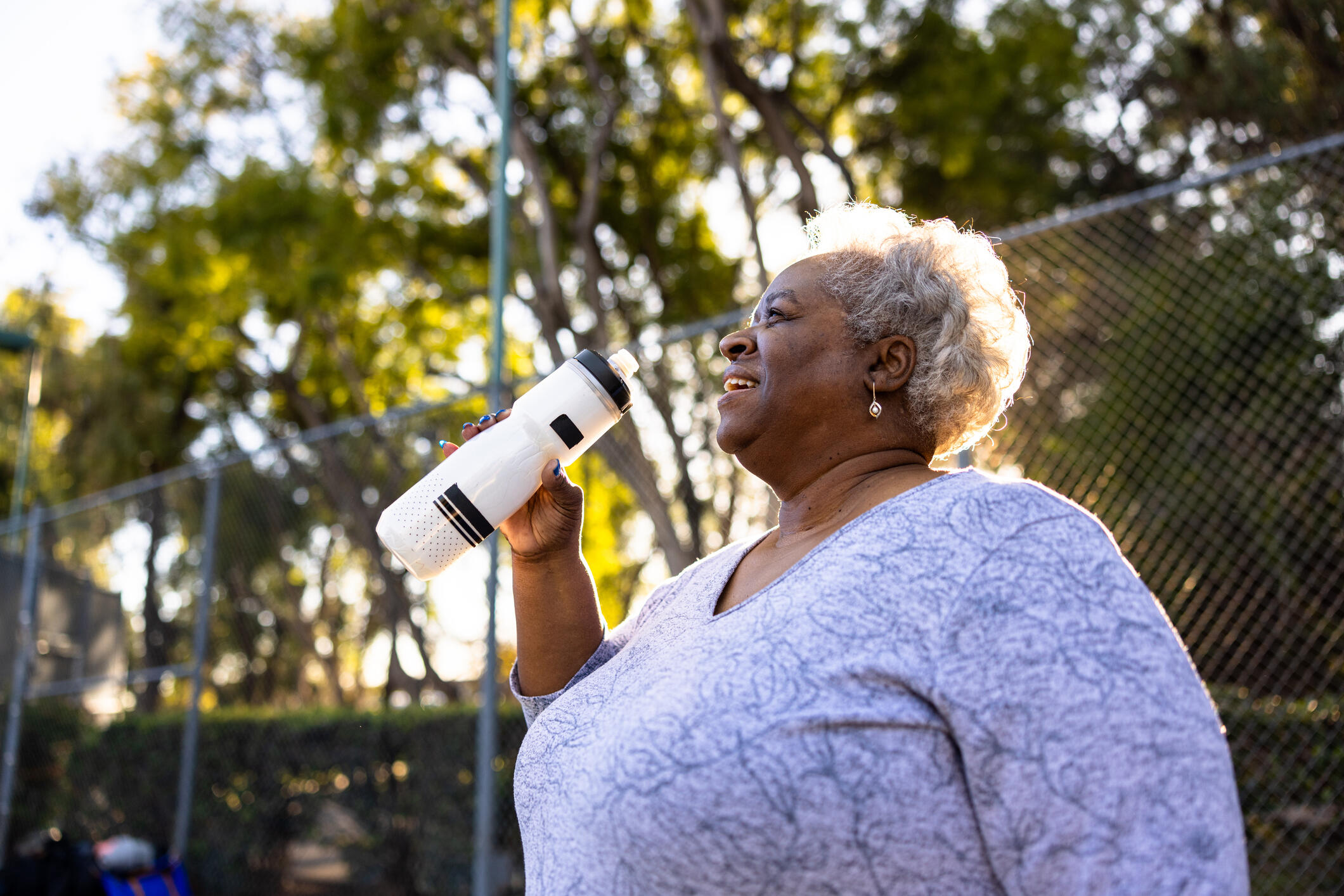 Older woman at the park drinking water. 
