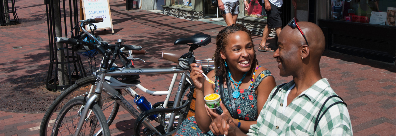 Two people smiling at each other while sitting on a bench on Church Street with bikes next to them.
