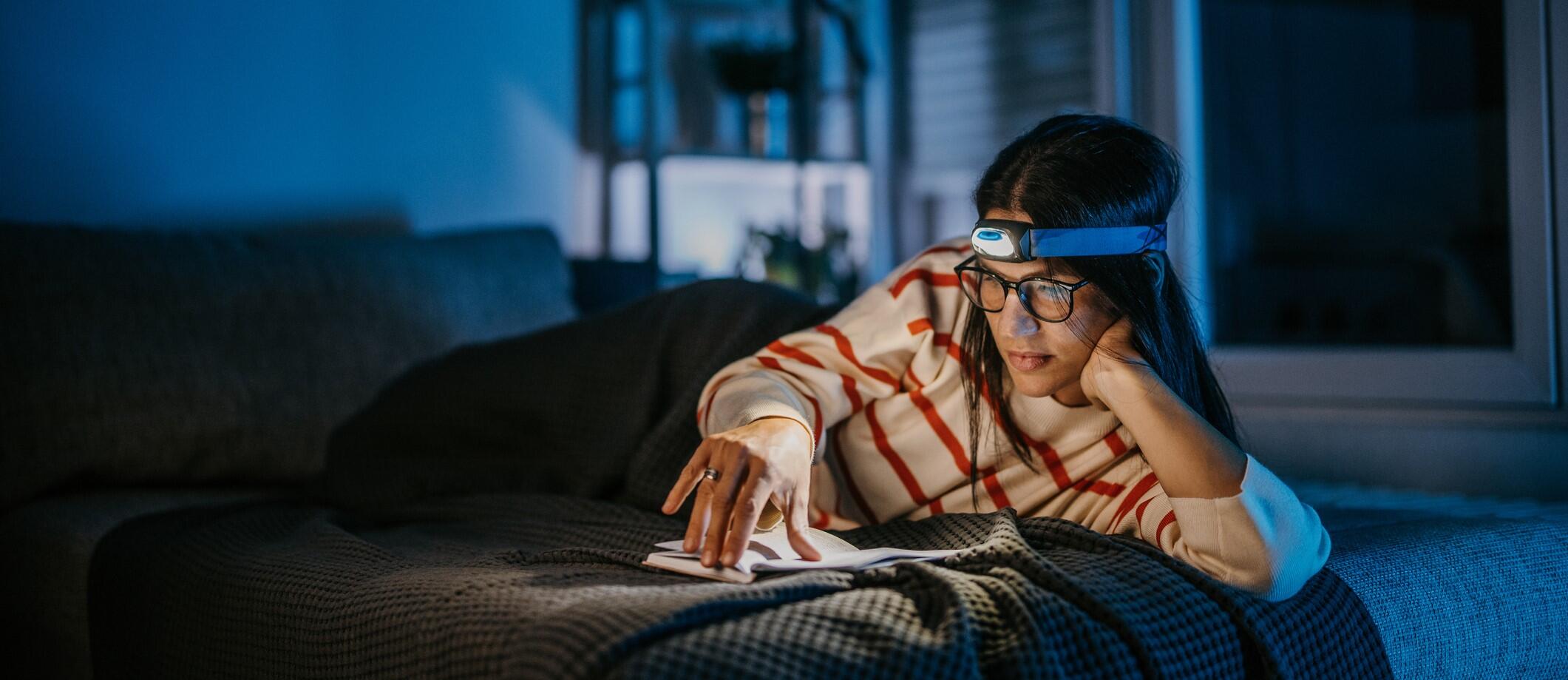 Teenager reading a book with a headlamp during a power outage. 