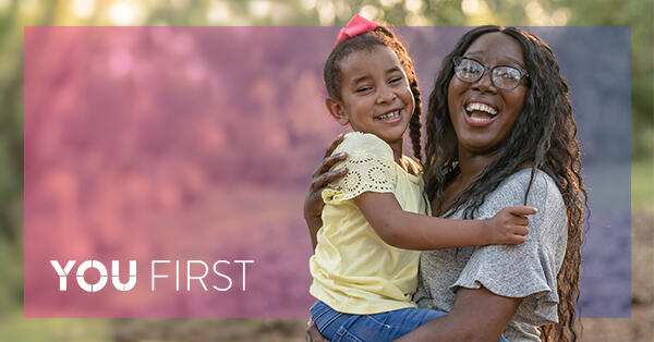 Woman holding child while both are smiling, with You First logo
