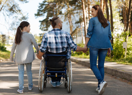 three people on walking path, including a child, man in a wheelchair and woman, holding hands