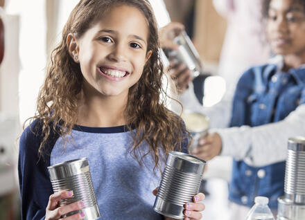 child holding unlabelled aluminum cans, bottled water and others in background, preparing for emergency