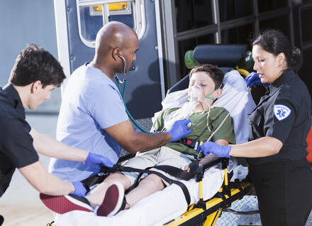 Doctor and paramedics helping boy lying on a stretcher outside an ambulance.