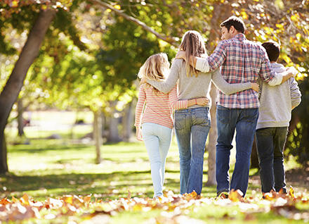Family of four walking away in a wooded park during fall. Family of four walking away in a wooded park during fall.