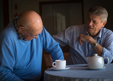 Two men talking at table with teapot and mug