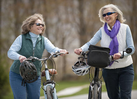 Two older women walking their bikes together