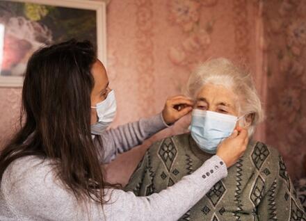 person helping older woman put mask on