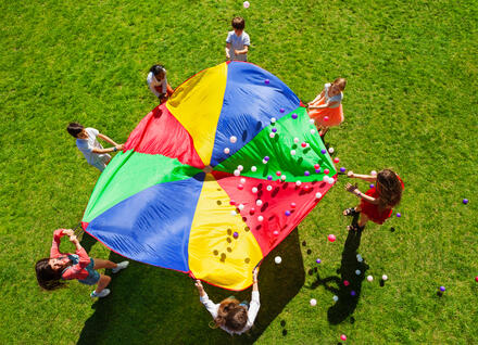 Kids playing with a parachute outdoors on a sunny summer day