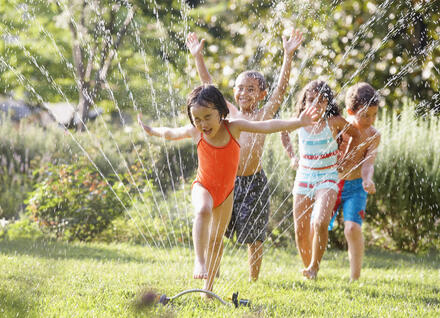 Happy kids running through a sprinkler on a summer day