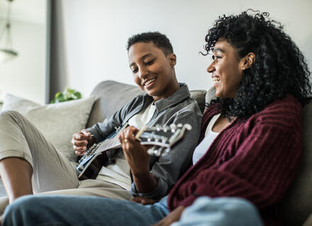 two people on couch, one playing guitar