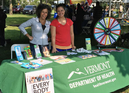 two people staff a Heath Dept table at Pride parade