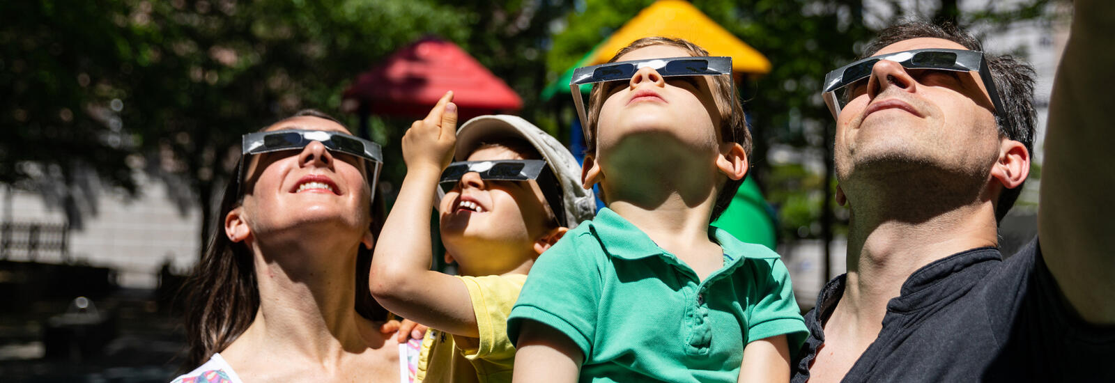 Parents and kids wearing eclipse glasses looking up at an eclipse.