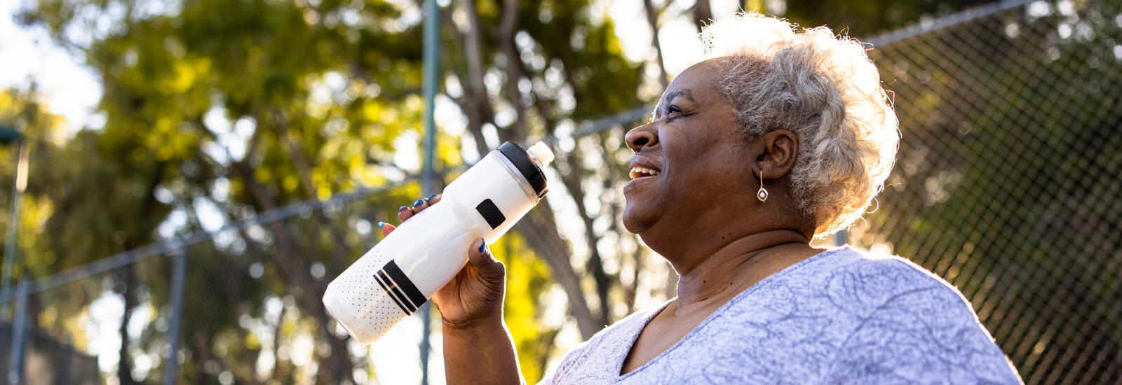 Older woman at the park drinking water. 