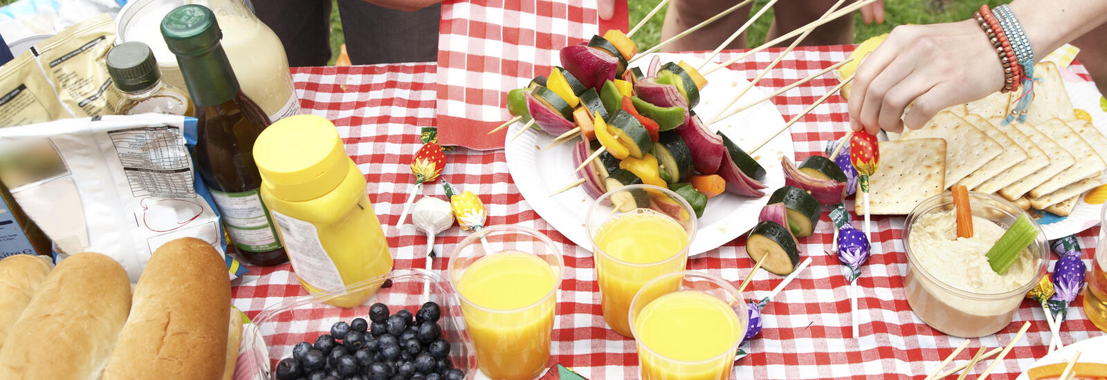A table full of color foods for a picnic. People's hands reaching for food.