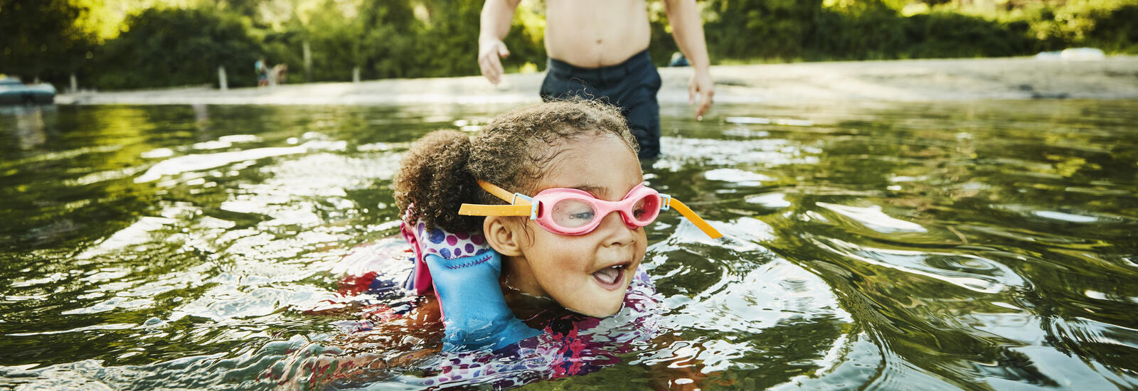 girl swimming in a lake with goggles and floaties