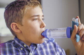 Photo of a boy breathing from an asthma inhaler with attached spacer device.
