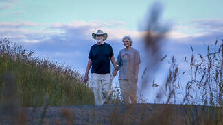 Photo of older man and woman walking hand-in-hand on a country road.