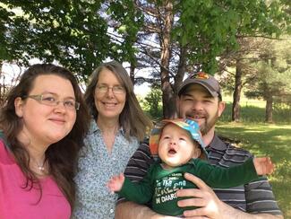 family with 3 adults and one baby gathered outdoors 